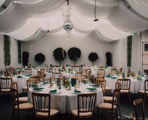 © Adrian Almasan | www.adrianalmasan.com Elegant Festzelt mit runden Tischen, weißen Tischdecken, Blumenarrangements und grünen Akzenten, dekoriert mit einem festlichen, drapierten Stoffdach und Kristallleuchtern, ideal für Veranstaltungen im Chadim.