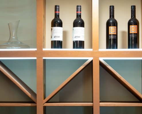 20220908_9280 Weinflaschen in einem dekorativen Regal im Restaurant Das Chadim, umgeben von warmem Licht und einem eleganten Glasdekantierer, ideal für Veranstaltungen und Feiern.