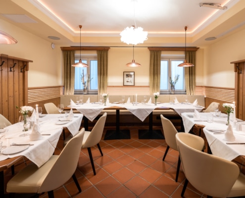 20220908_9307 Gemütlicher Essbereich im Stüberl „Friedrich-Adler“ mit gedeckten Tischen, eleganten Stühlen und warmem Licht, ideal für Familienfeiern und kleinere Veranstaltungen.