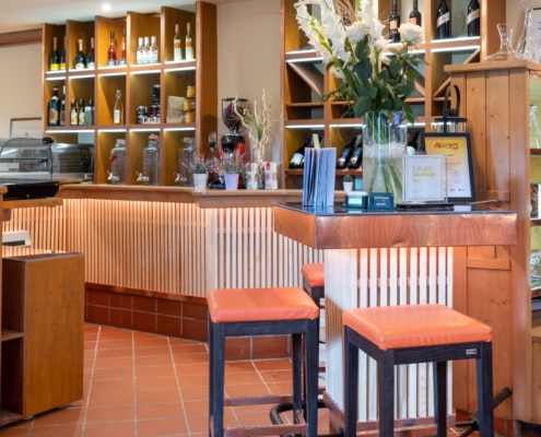 20220908_9332 Gemütlicher Barbereich im Lokal Das Chadim mit Holzregalen, Weinflaschen, Blumenarrangement und orangefarbenen Barhockern, ideal für Veranstaltungen und Feiern.