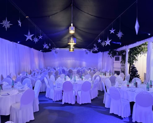 20231124_162116139_iOS Festzelt im Chadim mit eleganten runden Tischen, weißen Stuhlhussen und blauer LED-Beleuchtung, dekoriert mit Sternen und einem stilvollen Kronleuchter, ideal für Veranstaltungen bis zu 120 Personen.