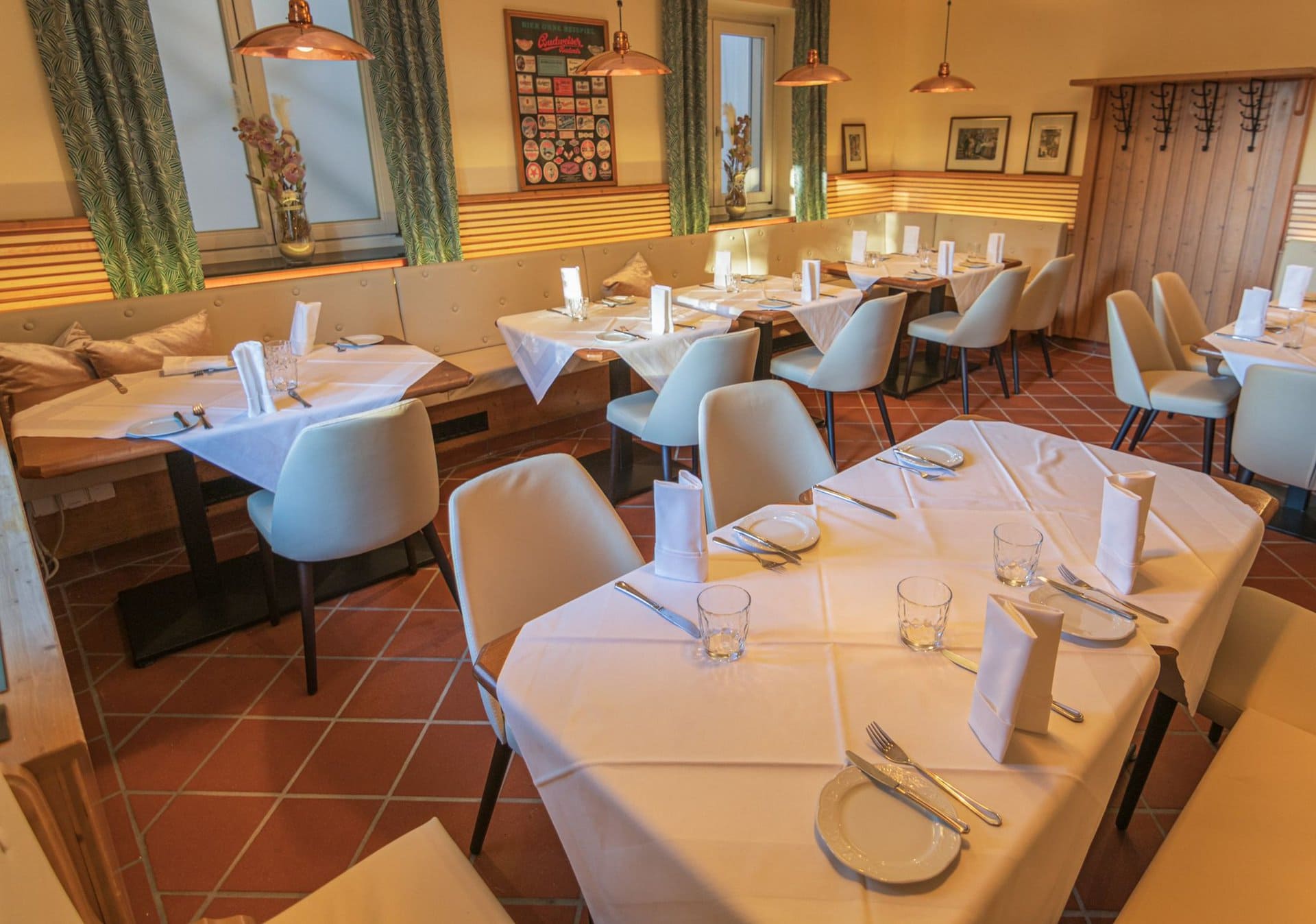 75e76ea2-7632-4fe6-b21b-db6070a30fe4 Gemütlicher Restaurantbereich mit Tischen und Stühlen, dekoriert mit weißen Tischdecken, Besteck und Gläsern, umgeben von Holz- und Lichtelementen, ideal für Veranstaltungen im Das Chadim.