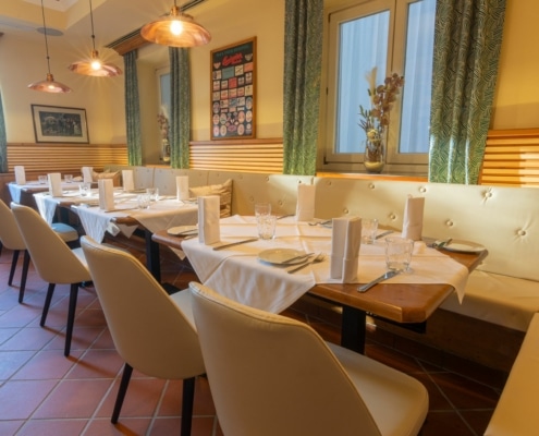 8f0c65a1-9d01-4d8c-b66b-15c99ad90137 Gemütlicher Speiseraum im Lokal Das Chadim mit eleganten Tischen, weißen Tischdecken und stilvollen Lampen, ideal für Veranstaltungen und Feierlichkeiten.