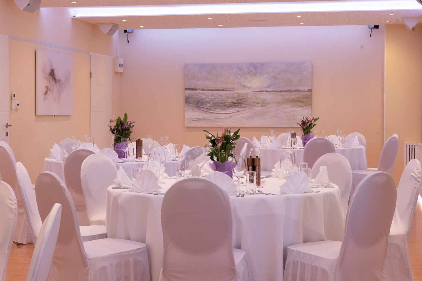 © Adrian Almasan | www.adrianalmasan.com Elegant Bankettraum mit runden Tischen, weißen Tischdecken, stilvollen Blumendekorationen und kunstvollem Wandbild, ideal für Veranstaltungen bei Das Chadim.