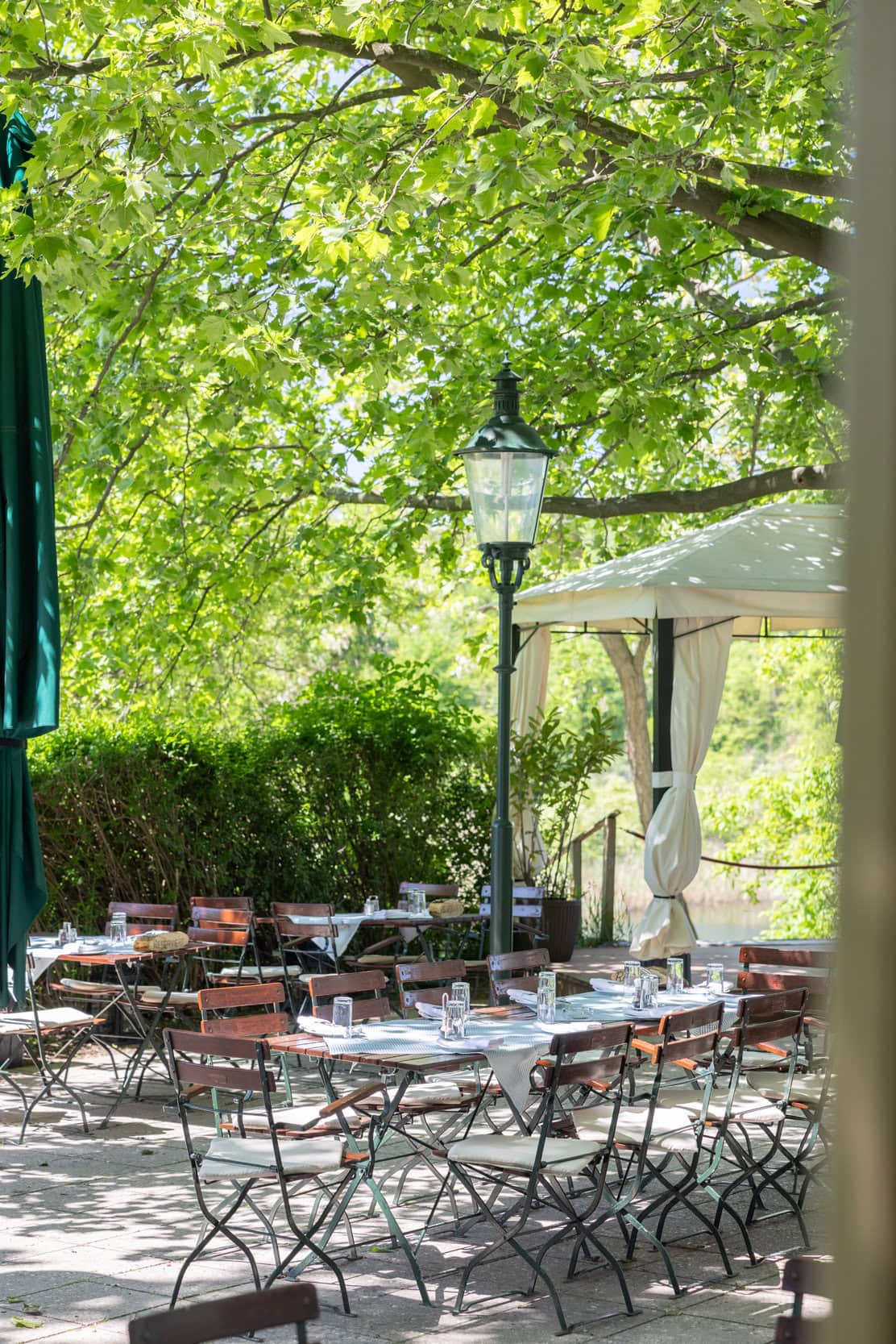 © Adrian Almasan | www.adrianalmasan.com Gastgarten im CHADIM mit schattigen Tischen und Stühlen unter Bäumen, ideal für entspannte Sommertage am See.