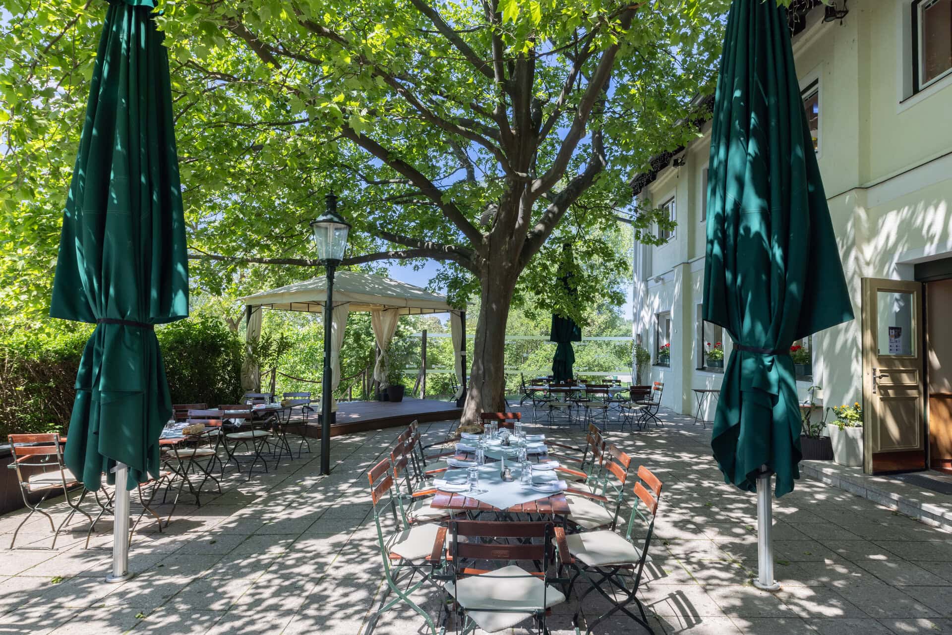 © Adrian Almasan | www.adrianalmasan.com Gastgarten von Das Chadim mit schattigen Bäumen, Tischen und Stühlen, Pavillon, ideal für Veranstaltungen und entspannte Sommermomente.