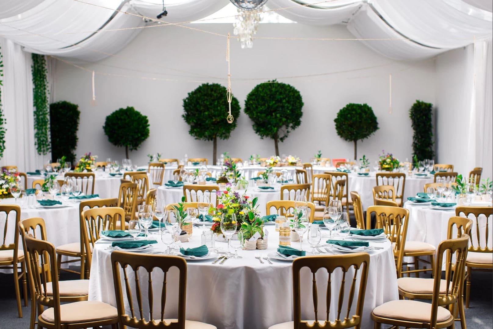 Festzelt_Almasan Festzelt von Das Chadim mit eleganten runden Tischen, weißen Tischdecken, grünen Servietten und floralen Mitteldekorationen, umgeben von dekorativen Bäumen, ideal für Veranstaltungen bis zu 120 Personen.