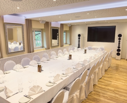 IMG_0754 Elegant gestalteter Bankettraum mit langen Tischen, weißer Tischdecke, dekorativen Servietten und HiFi-Lautsprechern, ideal für Feiern und Events im Das Chadim.