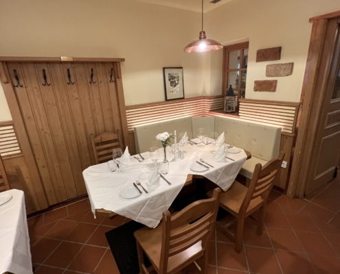 IMG_5539 Gemütlicher Essbereich im Restaurant Das Chadim mit Holzverkleidung, Tisch für vier Personen, eingedeckt mit Besteck und Gläsern, und Blick auf die Wand mit Garderobe und Dekoration.