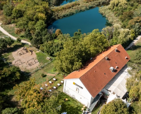 Kopie von Kopie von 20220909_9358 Luftaufnahme des Das Chadim Veranstaltungsortes mit Blick auf den Garten, Spielplatz und angrenzenden Gewässern, umgeben von üppigem Grün.