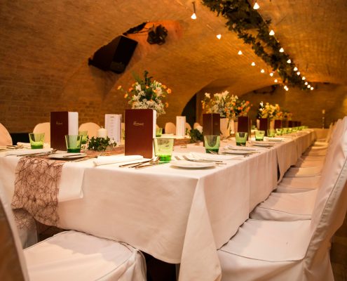Tafel_Gewölbe_Hochzeit_vh Elegant gedeckter Tisch im historischen Gewölbe von Das Chadim, umgeben von Blumenarrangements und LED-Beleuchtung, ideal für Veranstaltungen und Feiern.